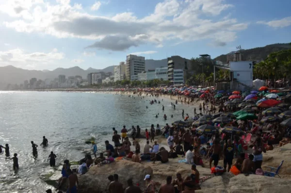 Vista ampla da Praia de Ipanema do alto, mostrando banhistas, guarda-sóis, ondas e prédios ao fundo
