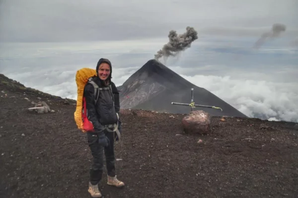 Hiker standing on Acatenango with Volcán de Fuego erupting in the background above the clouds