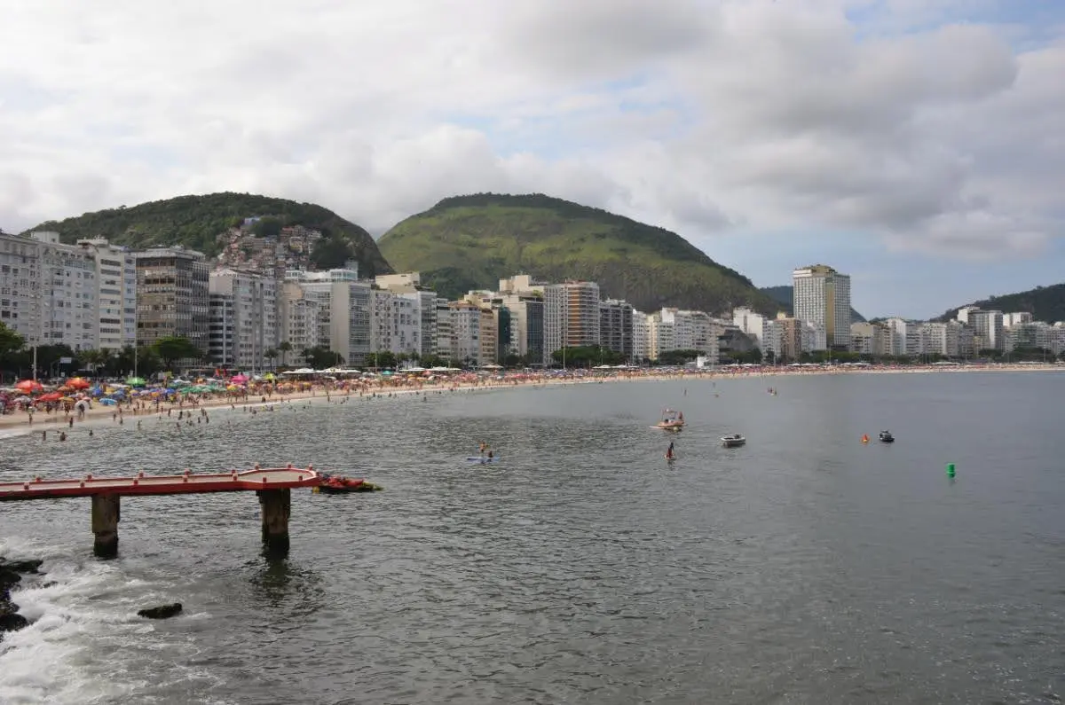 Panoramic view of Copacabana Beach in Rio de Janeiro from the fort’s edge, showing swimmers, gentle waves, and the city’s iconic arc of sand backed by high-rise buildings and lush hills.