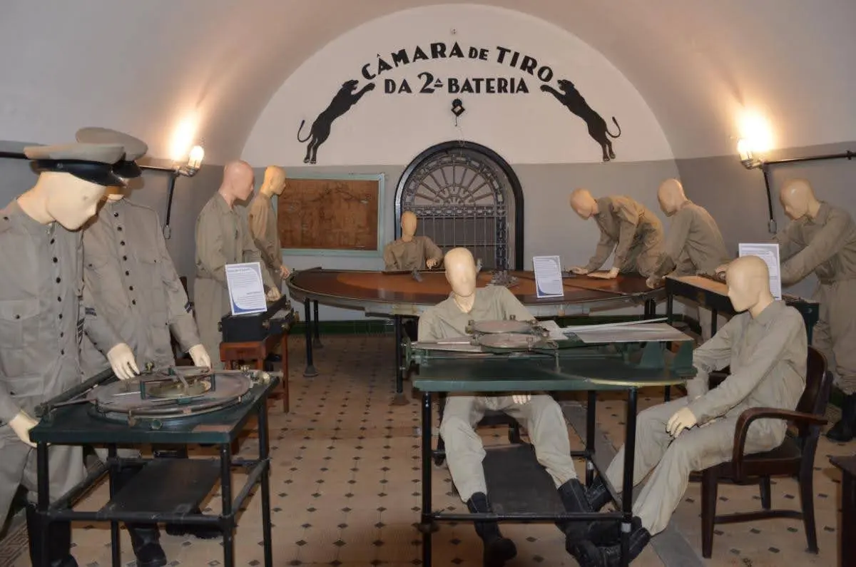 Military exhibit inside Fort Copacabana’s turret bunker featuring mannequins dressed as soldiers operating artillery, depicting how Brazilian forces managed the space during its active use.