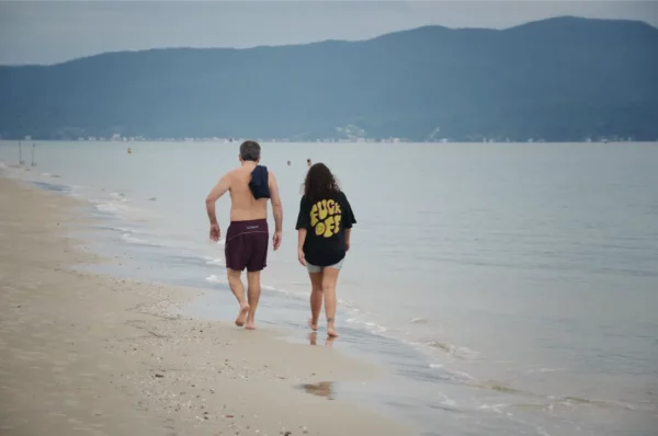 girl with a t-shirt saying "fuck off" in the back walking along a calm beach in brazil