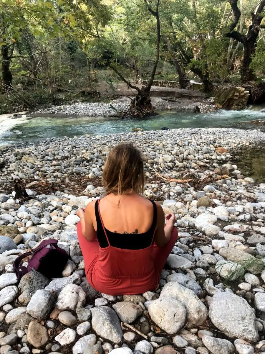 girl Meditating by river in forest of central evia island in greece