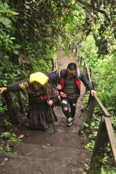 guy helping old lady up a steep muddy stairway at lake chicabal in guatemala