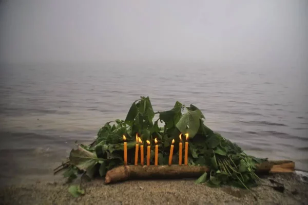 A naturalistic lakeside offering—fresh leaves, branches, and lit candles arranged in quiet reverence along the misty shore of Laguna Chicabal.