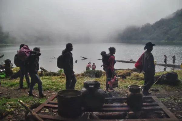 Pilgrims walking in front of platform with steaming kettles on shore of laguna chicabal