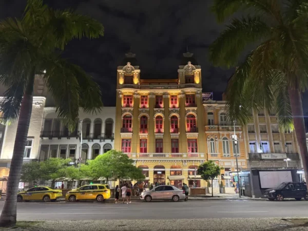 Historic colonial building illuminated at night in the Lapa neighborhood of Rio de Janeiro, framed by tall palm trees and vibrant street life, capturing the district’s architectural charm and festive energy.