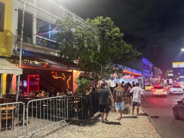 Locals and tourists gather at outdoor tables along a brightly lit street in Lapa, Rio de Janeiro, lined with bars, music, and vibrant nightlife activity, setting the stage for an energetic night out.
