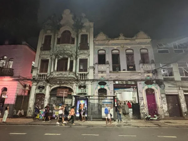 A grand historic building in Lapa, Rio de Janeiro, lit with warm pink and orange spotlights that enhance its ornate façade and nighttime presence, emphasizing the district’s architectural elegance.