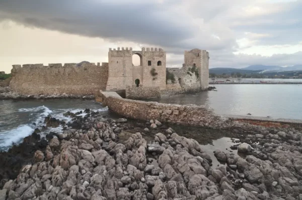 Panoramic coastal view of Methoni in Messinia, Greece, with the Ionian Sea, rocky shoreline, and the medieval Methoni Castle extending into the water.