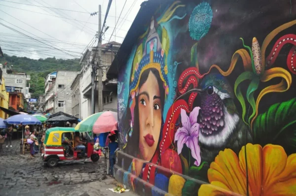Colorful street mural in San Pedro La Laguna, Lake Atitlán, Guatemala — depicting a Maya-style woman, hummingbird, and flowers on an alley wall.