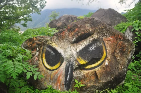 Owl face painted on a boulder at Las Piedras, surrounded by greenery above Lake Atitlán