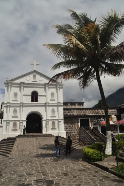 Whitewashed parish church in San Pedro La Laguna, with a palm tree and stone steps in the foreground.