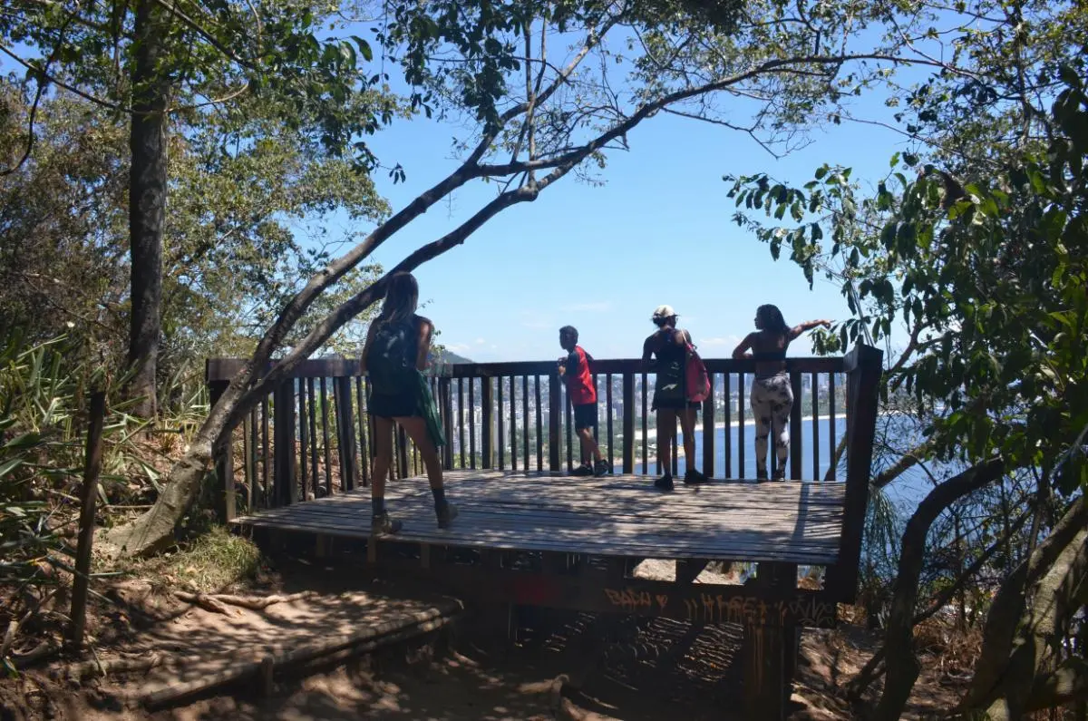 Group of hikers standing on a wooden viewing platform on col between Morro da Urca and Sugarloaf overlooking botafogo bay