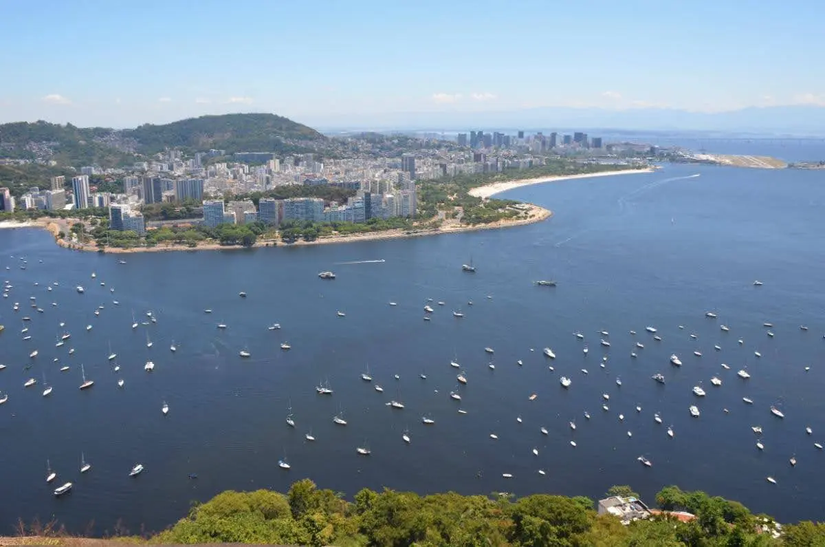 Aerial view of Botafogo Bay filled with small sailboats near the Urca neighborhood, backed by green hills and a cloudless sky in Rio de Janeiro