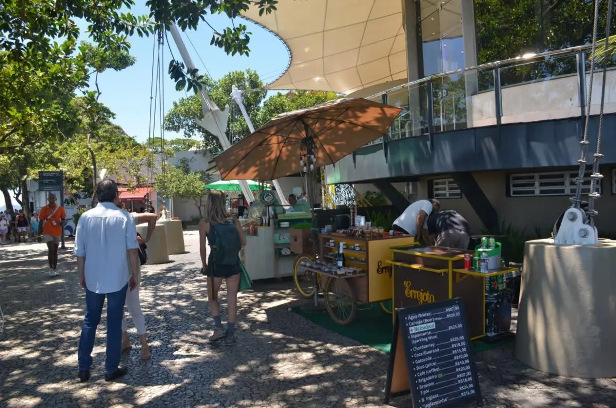 Open-air refreshment area with tables, umbrellas, and food stands offering drinks and snacks at the top of Morro da Urca in Rio de Janeiro