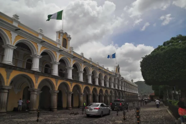 Long colonial arcade of the Palacio de los Capitanes in Antigua Guatemala, with flags, arches, and people walking along the cobblestone street