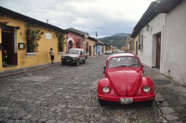 Red vintage Volkswagen Beetle parked on a cobblestone street in Antigua Guatemala, with colorful colonial houses in the background