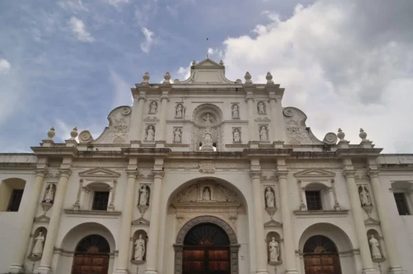 White baroque façade of the Cathedral of San José in Antigua Guatemala, with statues and cloudy sky above