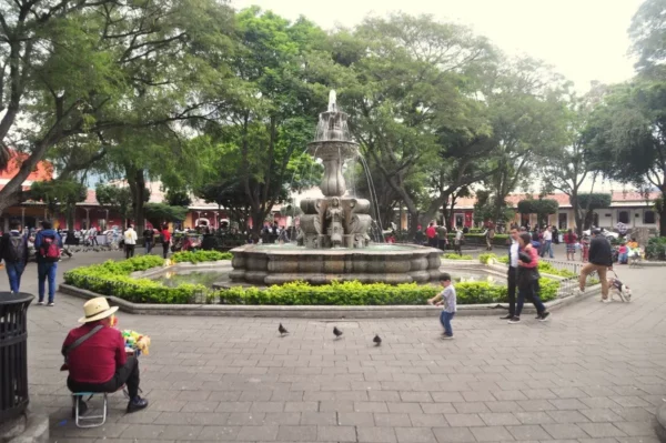 Baroque fountain in Parque Central in Antigua Guatemala, surrounded by trees, locals, and visitors in the main square