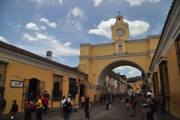 Santa Catalina Arch in Antigua Guatemala, with people walking along the cobblestone street and Volcán de Agua in the background