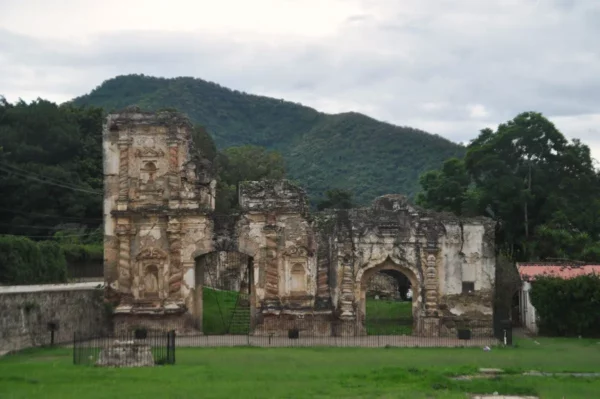 Ruins of the Iglesia de la Candelaria in Antigua Guatemala, with a crumbling stone façade, grassy courtyard, and green hills in the background