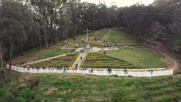 View of Cerro de la Cruz viewpoint above Antigua Guatemala, with people walking around the cross and terraced gardens surrounded by trees