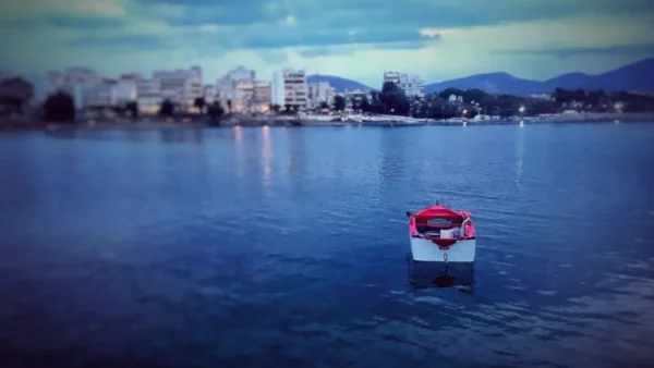 Colourful boat anchored in calm waters with Chalkis buildings and mountains in the background, capturing the tranquil evening scene.