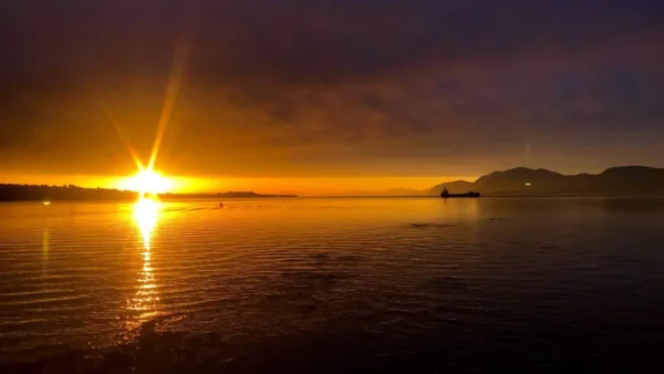 Golden sunrise reflecting on calm waters near Chalkis, Euboea, Greece, with silhouettes of distant hills.