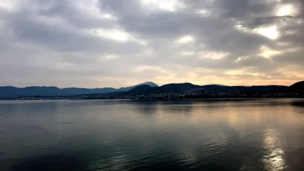 Serene waters reflect muted clouds and distant hills near Chalkis, Euboea, Greece, capturing a tranquil landscape at twilight.