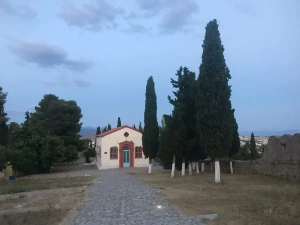 Charming cypress trees line the pathway leading to a quaint white chapel in Chalkis, Euboea, Greece.