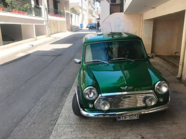 Classic green Mini Cooper parked on a narrow street in Chalkis, Euboea, Greece, surrounded by local buildings and vibrant colors.