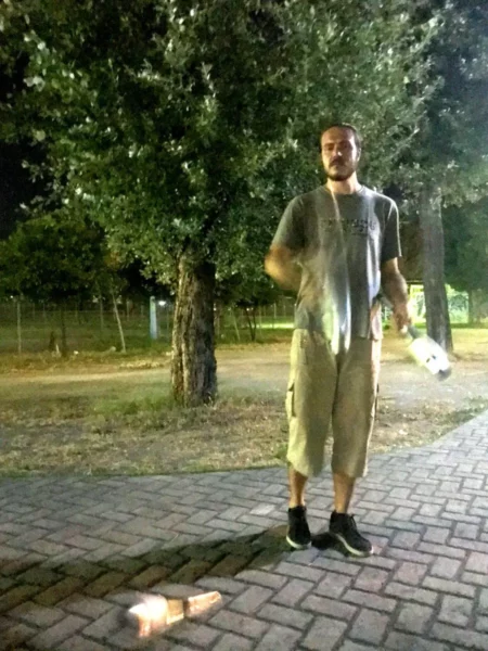 A juggler performing at night among trees in Chalkis, Euboea, Greece, with a relaxed park setting and brick pathway.