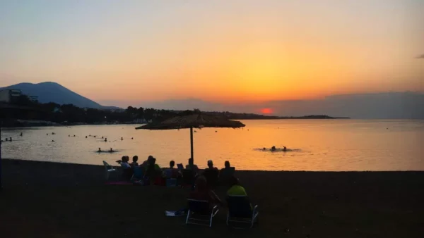 Sunset over the calm waters in Chalkis, Euboea, Greece, with silhouettes of people enjoying the beach.