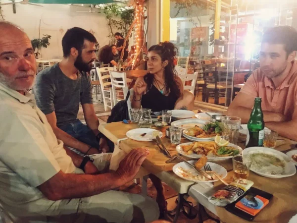 Enjoying a lively dinner with friends, surrounded by plates of food and drinks at a cozy eatery in Chalkis, Euboea, Greece.