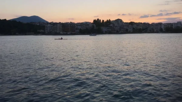 Serene sunset over Chalkis, Euboea, Greece, with a silhouette of a lone kayaker paddling across calm waters.