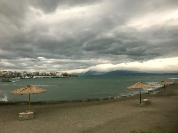Chalkis features sandy shores with straw umbrellas under a moody sky, overlooking the calm waters of Euboea, Greece.