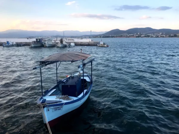Traditional fishing boat anchored in the tranquil waters of Chalkis, Euboea, Greece, with distant hills and a harbor visible.