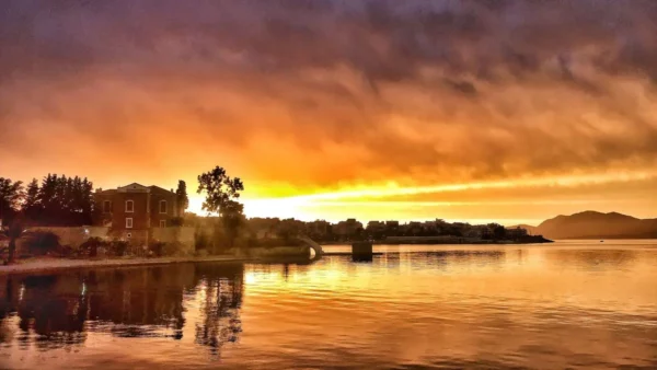 Vibrant sunset over the calm waters of Chalkis, Euboea, Greece, reflecting warm oranges and yellows against the scenery.