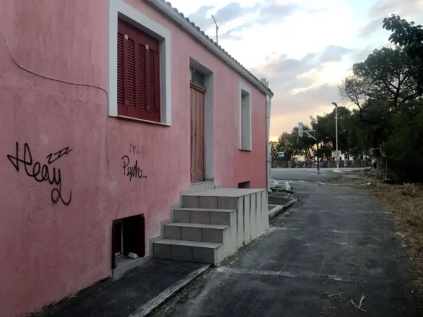 Charming pink building with wooden door and graffiti, set along a quiet path in Chalkis, Euboea, Greece.