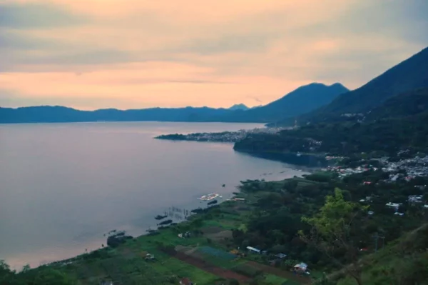 Sunset over Lake Atitlán in Guatemala, showcasing the tranquil waters, lush greenery, and mountains in the distance.