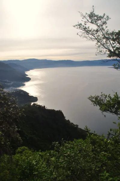 Sunlight glimmers on the calm waters of Lake Atitlán, framed by lush greenery and distant hills in Guatemala.