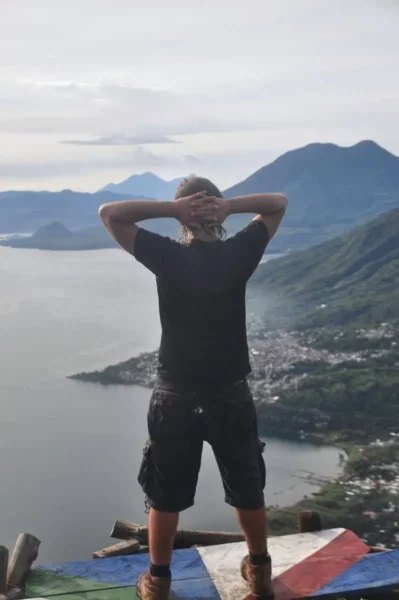 A view from Indian Nose overlooking Lake Atitlán and surrounding mountains, with a person enjoying the scenic landscape.