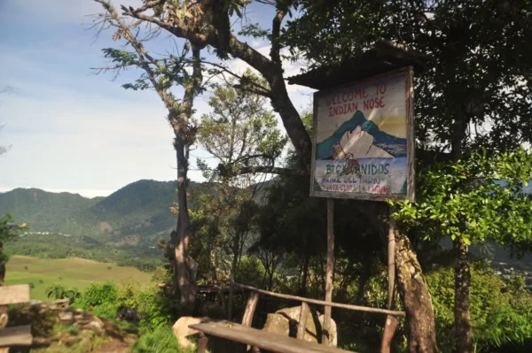 Stunning view of Lake Atitlán framed by trees, featuring a colorful sign and distant mountains under bright blue skies.