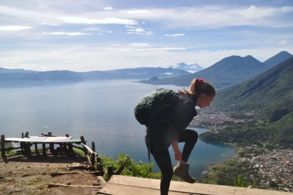 Hiker adjusting boots with the stunning Lake Atitlán and mountains in the background under a clear sky.