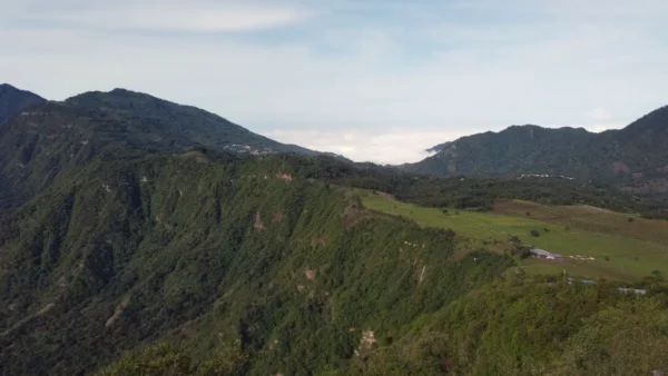 Lush green hills roll down to the serene waters of Lake Atitlán, surrounded by distant mountains and a clear blue sky.