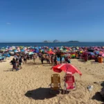 Brightly colored beach umbrellas packed tightly together on the sand with crowds enjoying the sun and sea