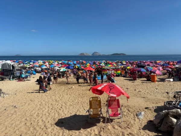 Guarda-sóis coloridos enfileirados na areia, lotada de banhistas curtindo o sol e o mar