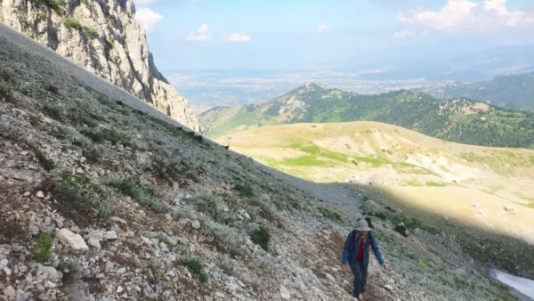 Hiker traverses the rocky slope of Mount Xerovouni, with lush green valleys and distant mountains in Euboea, Greece.