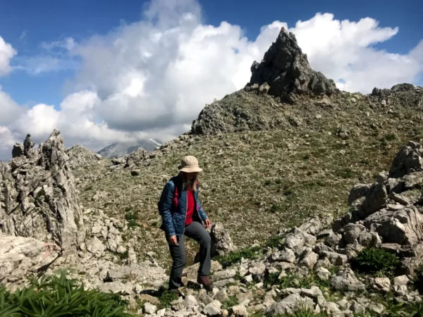 Hiker navigating rocky terrain at Mount Xerovouni, surrounded by rugged landscape and cloud-dotted blue sky in Euboea, Greece.