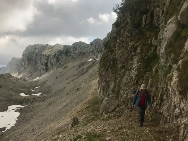 Hiker traversing rocky terrain near Mount Xerovouni, showcasing rugged cliffs and patches of snow in Euboea, Greece.